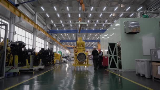 ロシアのマガダン 2019年8月15日 重機のエンジンやギアボックスを復元するための工場 ヘルメットの労働者はクレーンでエンジンを運ぶ — ストック動画