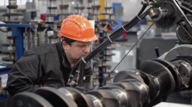 Kasklı bir işçi özel bir makinenin arkasında çalışır. Ağır ekipmanlar için motor ve şanzıman yenileme fabrikası.