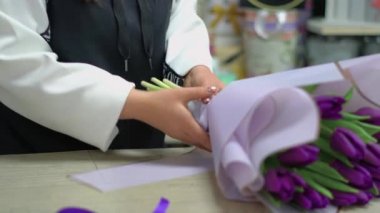 Çiçekçi bir buket mor lale topluyor. Kız çiçekleri hediye paketine sarar..