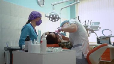Dişçi randevusundaki hasta. Dişçi ve asistanı askeri üniformalı hastayı tedavi ediyorlar. Diş hekimi dişi doldurur..