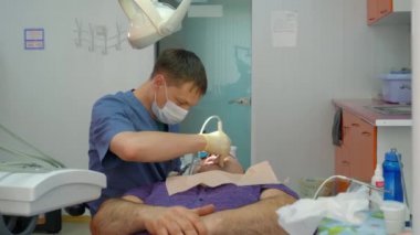 Dişçi randevusundaki hasta. Tıbbi önlüklü bir dişçi bir hastayı, yetişkin bir adamı tedavi eder..