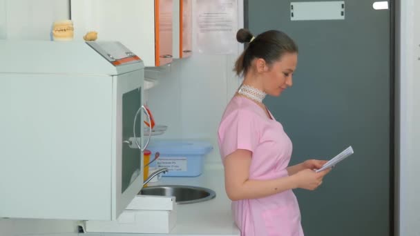 一位穿着性感粉色外套的年轻漂亮的女医生站在她的办公室里看她的病历 她把头转向病人身边 — 图库视频影像