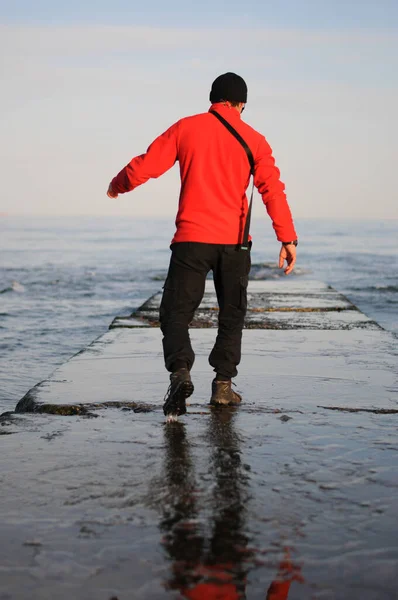 Man standing back view on the sea shore. A man looking ahead. Waves hitting the shore. Gloomy, cloudy sky.Man in red sweater.