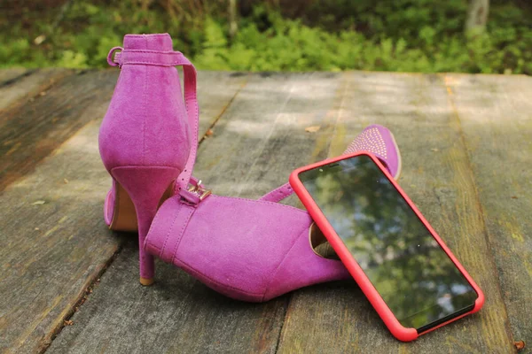 Kadın fuşya ayakkabıları ve ahşap bir masada akıllı telefon..