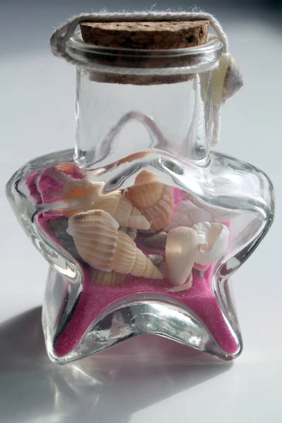 Tatil köyünden bir hatıra. Penceresinde deniz kumu ve deniz kabukları olan cam bir şişe..