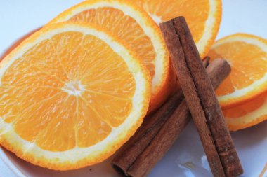 Turuncu portakallar, beyaz arka planda dilimlenmiş halkalar ve tarçın çubukları..