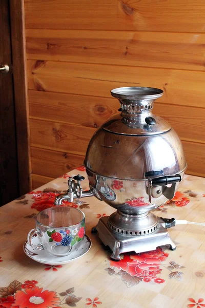 Parlak bir semaver ve masada şeffaf bir cam bardak..