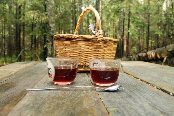 Hasır bir sepetin arka planında, tahta bir masanın üzerinde çay bardakları. Sokakta çay partisi..