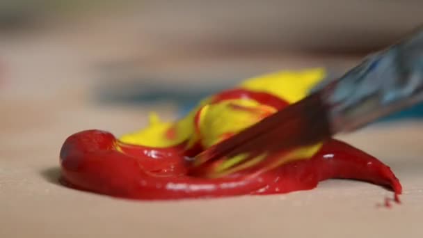 Mezcla de pintura al óleo rojo y amarillo con un pincel — Vídeo de stock