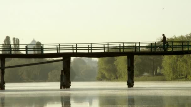 Férfi kerékpár, gyalogos híd a folyón — Stock videók