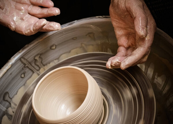 Hands of the master potter and vase of clay on the potters wheel