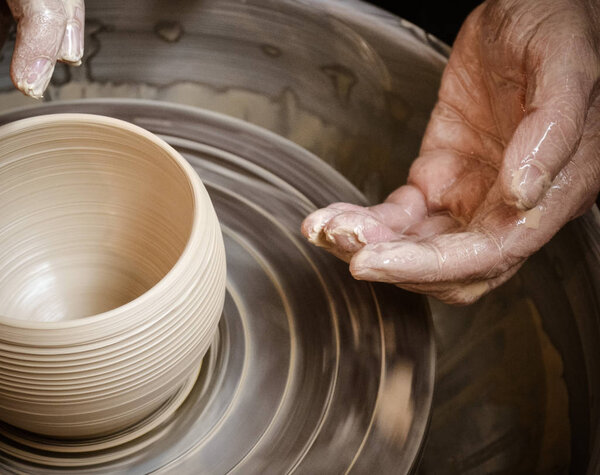 Hands of the master potter and vase of clay on the potters wheel