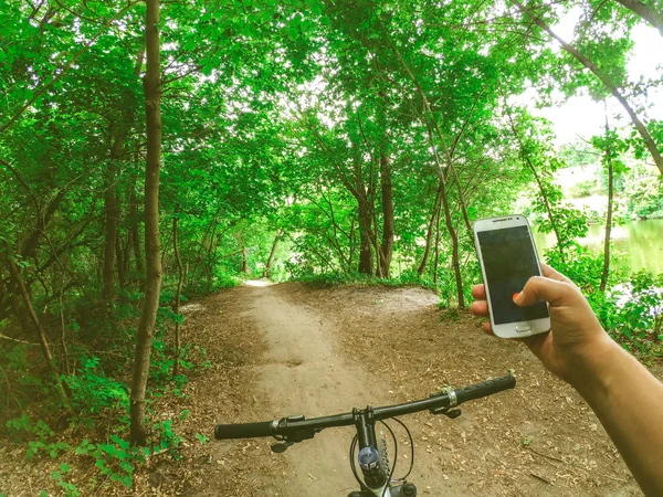 Fahrradfahrer steht mit Handy im Wald auf einem Feldweg — Stockfoto