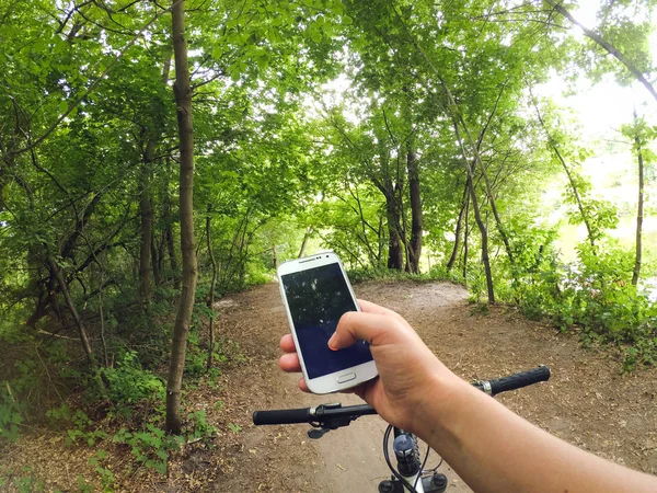 Fahrradfahrer steht mit Handy im Wald auf einem Feldweg — Stockfoto