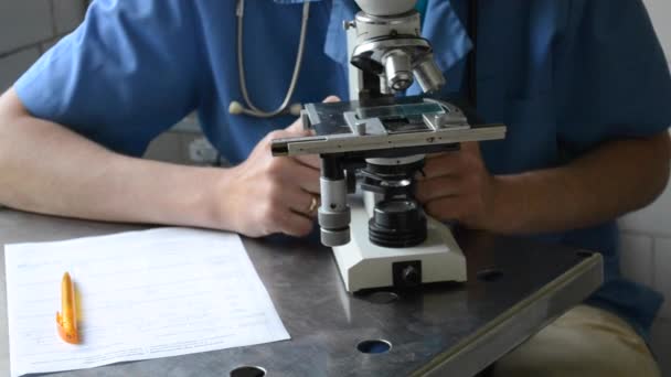 Médico masculino mira en un microscopio de cerca — Vídeo de stock