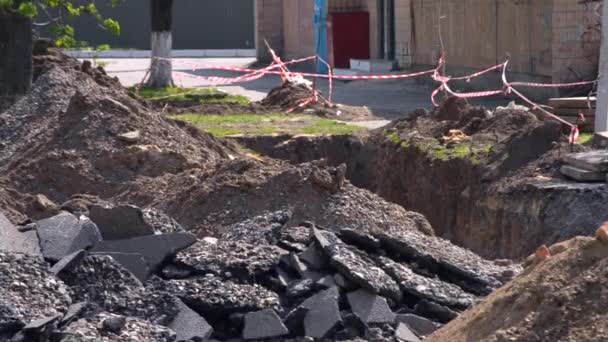 Pedaços de asfalto quebrado e um poço escavado com uma fita protetora vermelho-branca — Vídeo de Stock