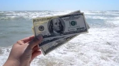 Kız, dalgaların arka planında 300 dolar tutuyor.