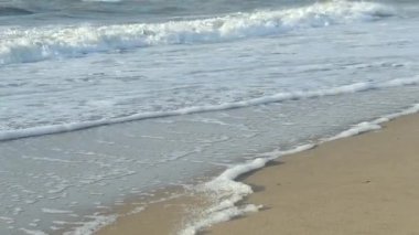 Suyun yüzeyi, kumsalda beyaz köpükle dalgalanır..
