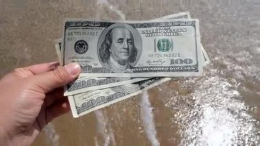 Deniz dalgalarının arka planında 300 dolarlık para tutan bir kız.