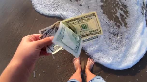 Flicka som håller en räkning på 300 dollar på bakgrunden av sand i havet — Stockvideo