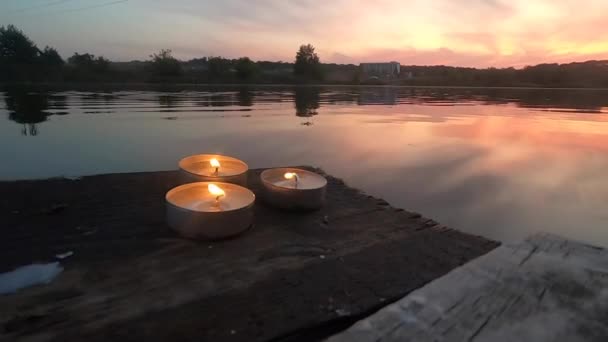Drie pil kaarsen liggen op de rand van een oude houten plank werf — Stockvideo