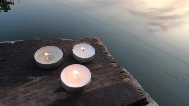 Drie pil kaarsen liggen op de rand van een oude houten plank werf — Stockvideo