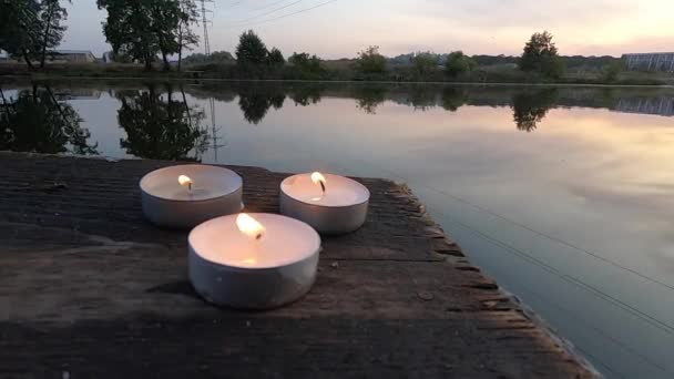 Drie pil kaarsen liggen op de rand van een oude houten plank werf — Stockvideo