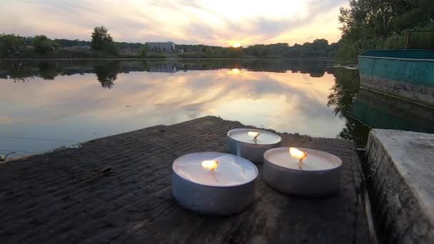 Drie pil kaarsen liggen op de rand van een oude houten plank werf — Stockvideo