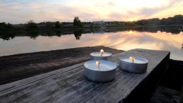 Drie pil kaarsen liggen op de rand van een oude houten plank werf — Stockvideo