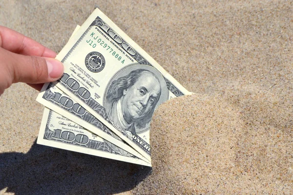 A girl takes out from the sand money notes of three hundred dollars.