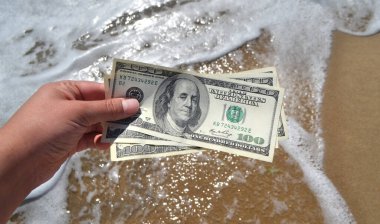 Deniz dalgalarının arka planında 300 dolarlık para tutan bir kız.
