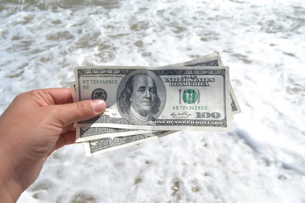 Girl holding money bill of 300 dollars on background of sea oceans