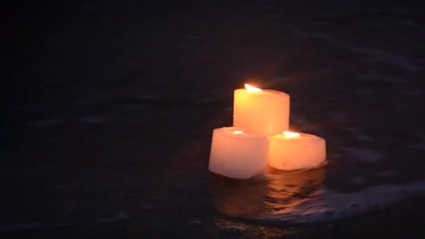 Tres pequeñas velas en la playa de arena cerca de las olas del mar ardiendo — Vídeos de Stock