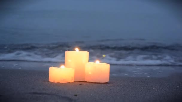 Three small candles on sandy beach near sea ocean waves burning — ストック動画