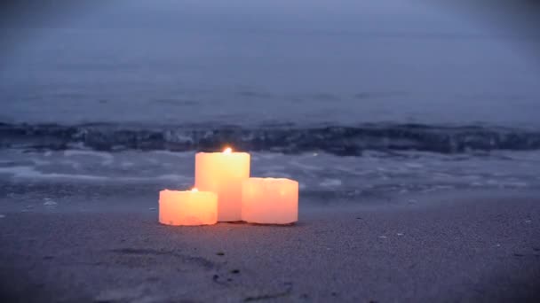 Три маленькие свечи на песчаном пляже возле морских океанских волн горящих — стоковое видео