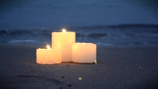 Три маленькие свечи на песчаном пляже возле морских океанских волн горящих — стоковое видео
