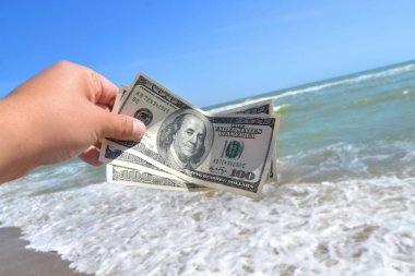Deniz dalgalarının arka planında 300 dolarlık para tutan bir kız.