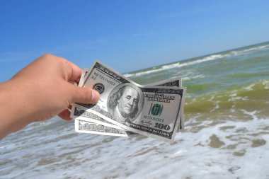 Deniz dalgalarının arka planında 300 dolarlık para tutan bir kız.