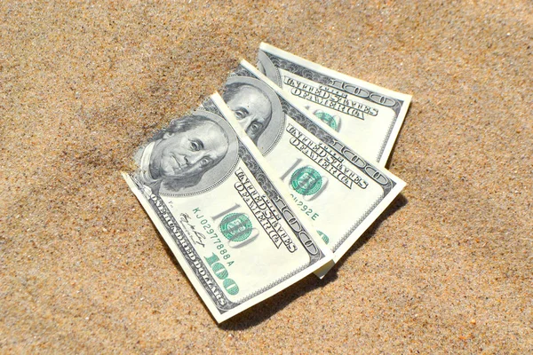 Money dolars half covered with sand lie on beach close-up.
