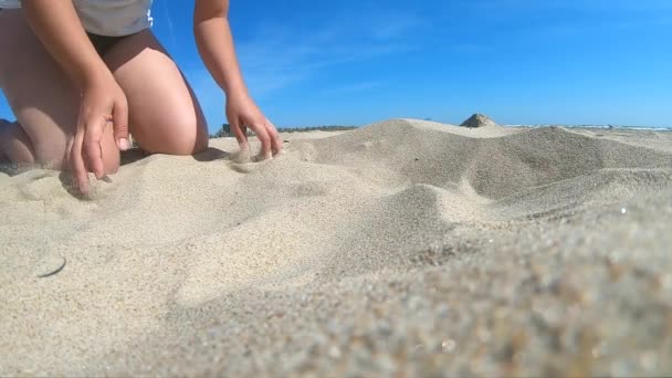 Sakta i backarna. Låg vinkel. Flickan plockar upp en handfull sand i handflatan — Stockvideo