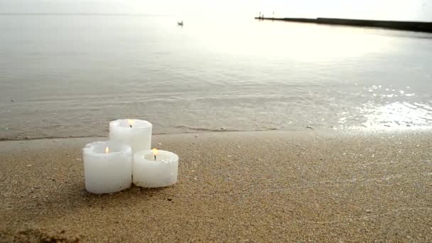 Tres pequeñas velas amarillas en la playa de arena cerca de las olas azules del mar — Vídeos de Stock