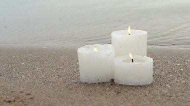 Mavi deniz dalgalarının yanındaki kumlu sahilde üç küçük sarı mum.