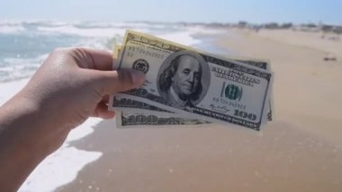 Deniz dalgalarının arka planında 300 dolarlık para tutan bir kız.