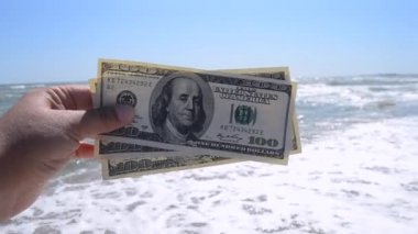 Deniz dalgalarının arka planında 300 dolarlık para tutan bir kız.