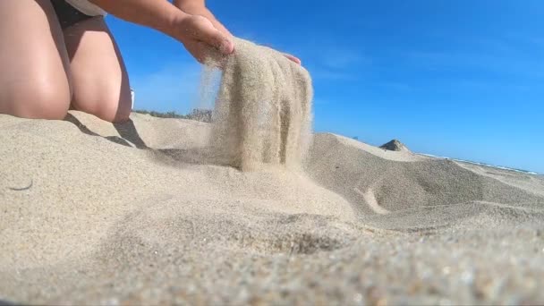 Langzame beweging. Lage hoek. Meisje pakt handvol zand in haar handpalm — Stockvideo