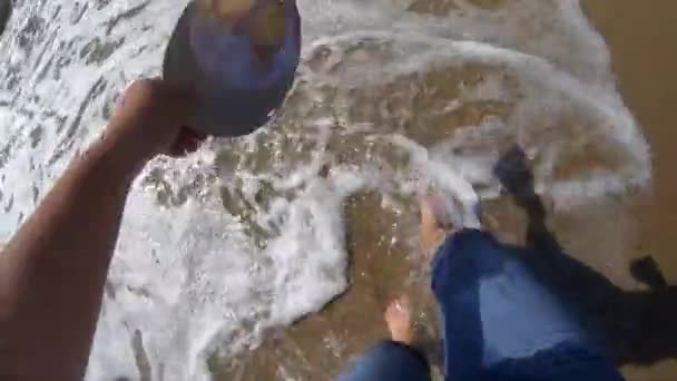 Het meisje is wandelingen in de buurt van de zee en golven rollen op haar voeten op het zandstrand in heldere zonnige dag. — Stockvideo