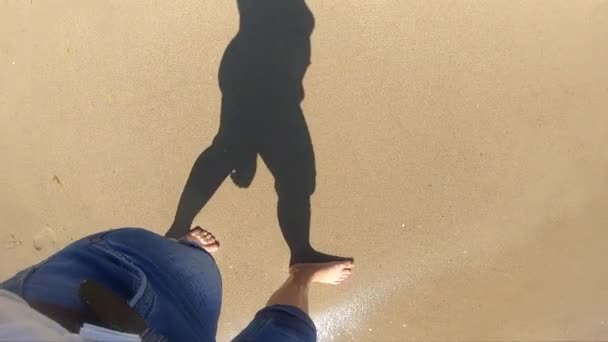 The girl is walks near sea and waves roll on her feet on sandy beach in bright sunny day. — Stock Video