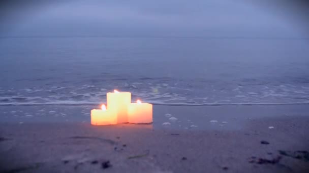 Tres pequeñas velas en la playa de arena cerca de las olas del mar ardiendo — Vídeo de stock