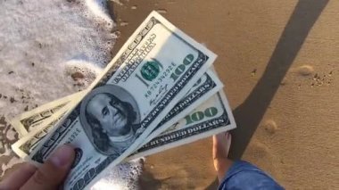Deniz dalgalarının arka planında 300 dolarlık para tutan bir kız.