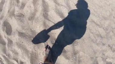 Sahilde kumsalda yürüyen bir kızın siyah gölgesi.
